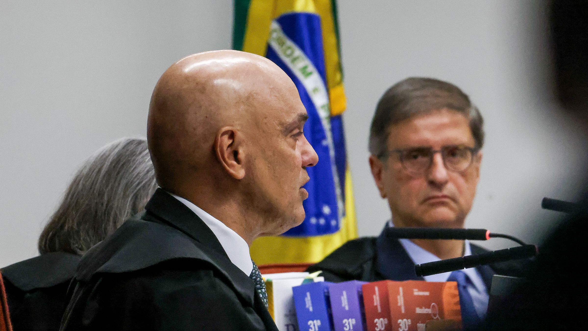 Alexandre de Moraes fala, observado por Paulo Gonet, durante o primeiro dia do julgamento de Jair Bolsonaro por tentativa de golpe de Estado.