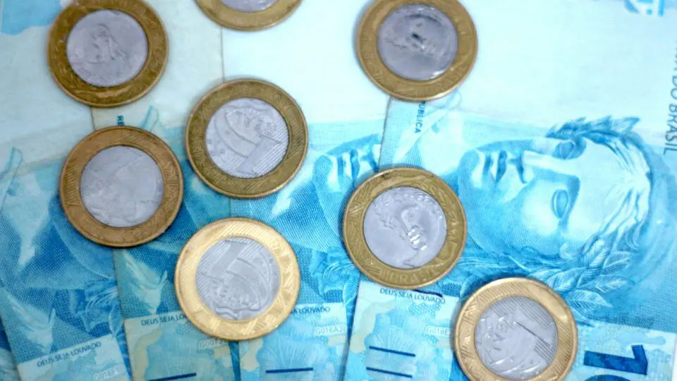 Moedas de um real junto com notas de cem reais.