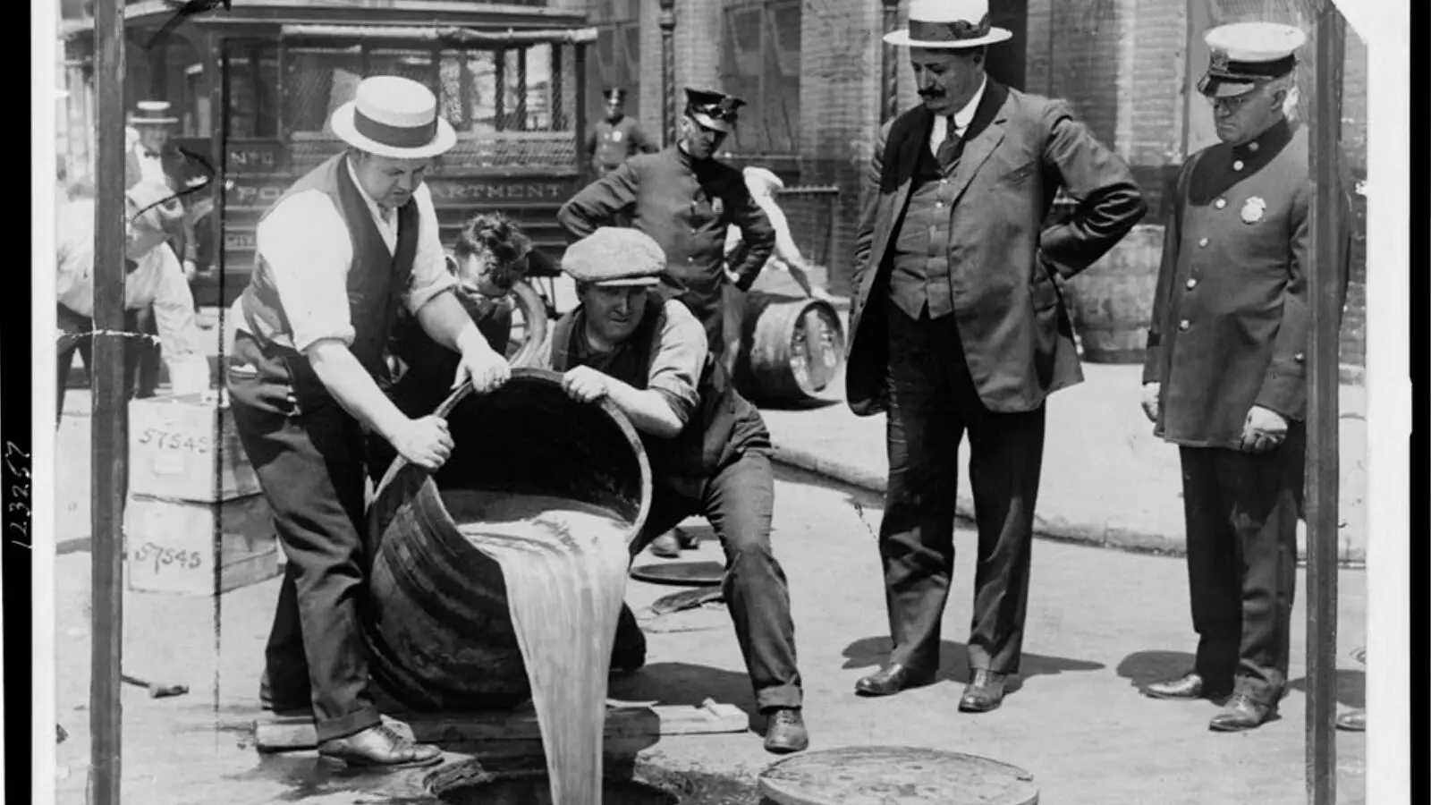 Observados por representante da polícia, funcionários jogam álcool no esgoto durante a era da Proibição em Nova York.