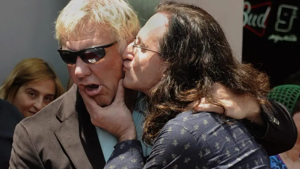 O serelepe Geddy Lee tasca um beijo na bochecha de Alex Lifeson