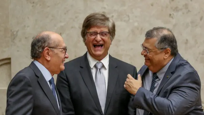 Procurador-Geral da República Paulo Gonet caminhando e sendo abordado por microfone em frente a evento internacional.