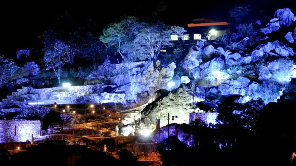À noite, a serra muda de tom. A iluminação cênica revela o Presépio Mãos de Deus, destacando as esculturas entre as rochas.