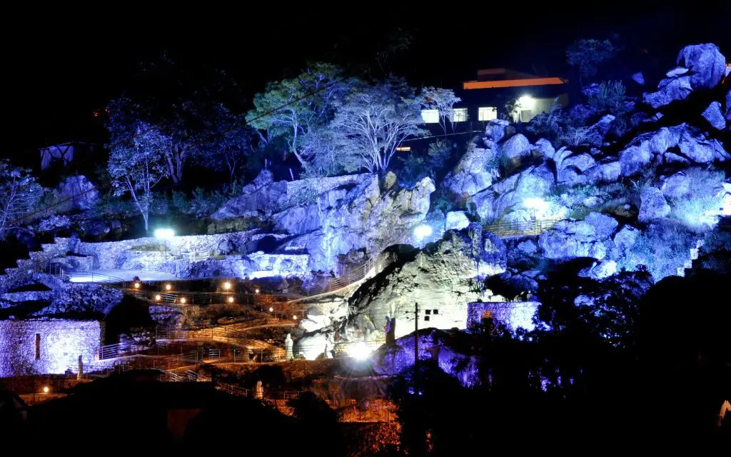 À noite, a serra muda de tom. A iluminação cênica revela o Presépio Mãos de Deus, destacando as esculturas entre as rochas.