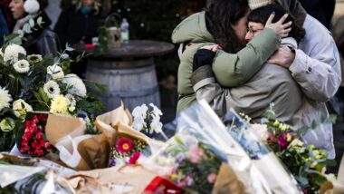 Pessoas prestando homenagens às vítimas com flores perto do local do incêndio no bar Le Constellation. Imagem referente a matéria