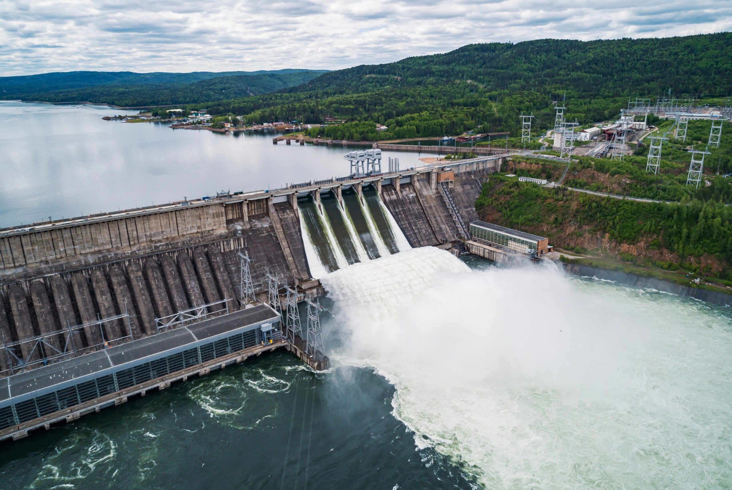 Usina hidrelétrica em operação, com vertedouro aberto e liberação de água, evidenciando a força da geração hídrica como base da energia firme no sistema elétrico brasileiro.