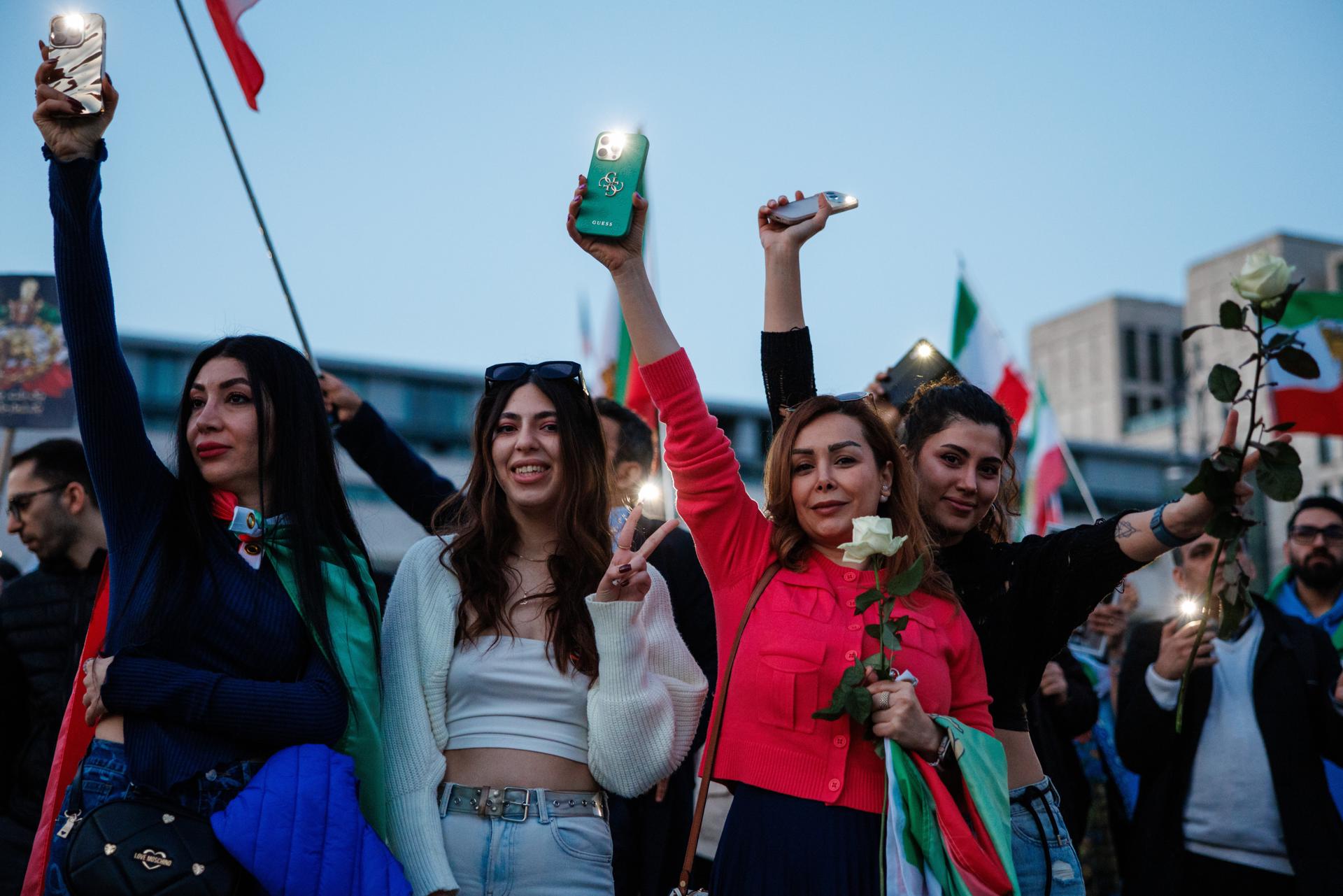 Participantes seguram flores e acendem as lanternas de seus smartphones, apontando-as para a embaixada dos EUA durante uma demonstração de apoio feita por iranianos exilados em frente à embaixada americana em Berlim, Alemanha, em 28 de fevereiro de 2026. A manifestação ocorreu sob o lema “Liberdade para o Irã”