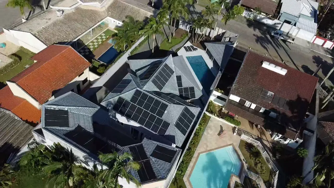 Infraestrutura Sustentável: Vista aérea de residência equipada com sistema de microgeração distribuída da Amicta Sole. A disposição estratégica dos painéis fotovoltaicos maximiza a captação solar de acordo com a inclinação do telhado, garantindo a máxima eficiência energética para o imóvel.