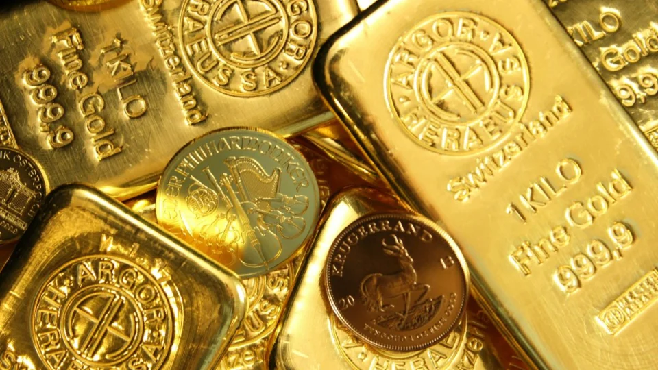 Barras de ouro com moedas de ouro, metais considerados mais seguros em meio a crises.