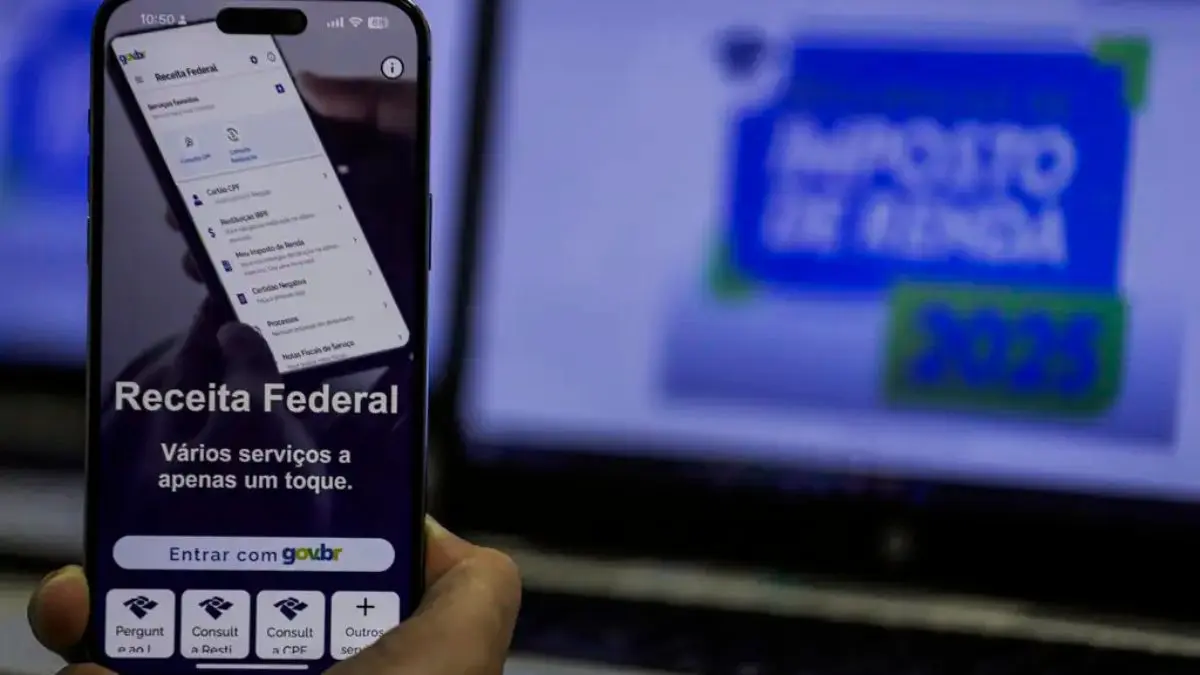 Celular e computador aberto no site oficial da Receita Federal, onde o CDB do Banco Master deve ser declarado no IR 2026.