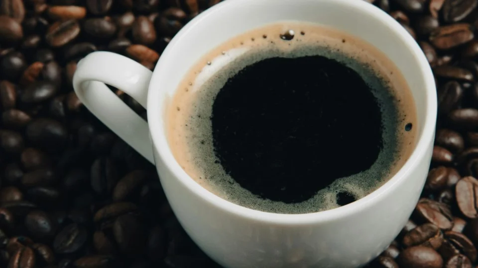 Xícara de café com grãos ao lado, que pode melhorar o humor.