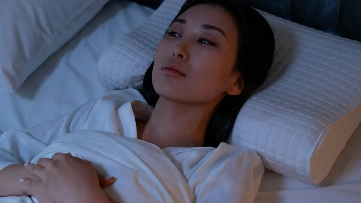 Mulher deitada na cama, de olhos abertos. Ela está com dificuldade para dormir.