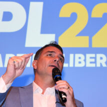 Flávio Bolsonaro com um microfone na mão apontando para frente e no fundo um painel escrito PL 22 Partido Liberal
