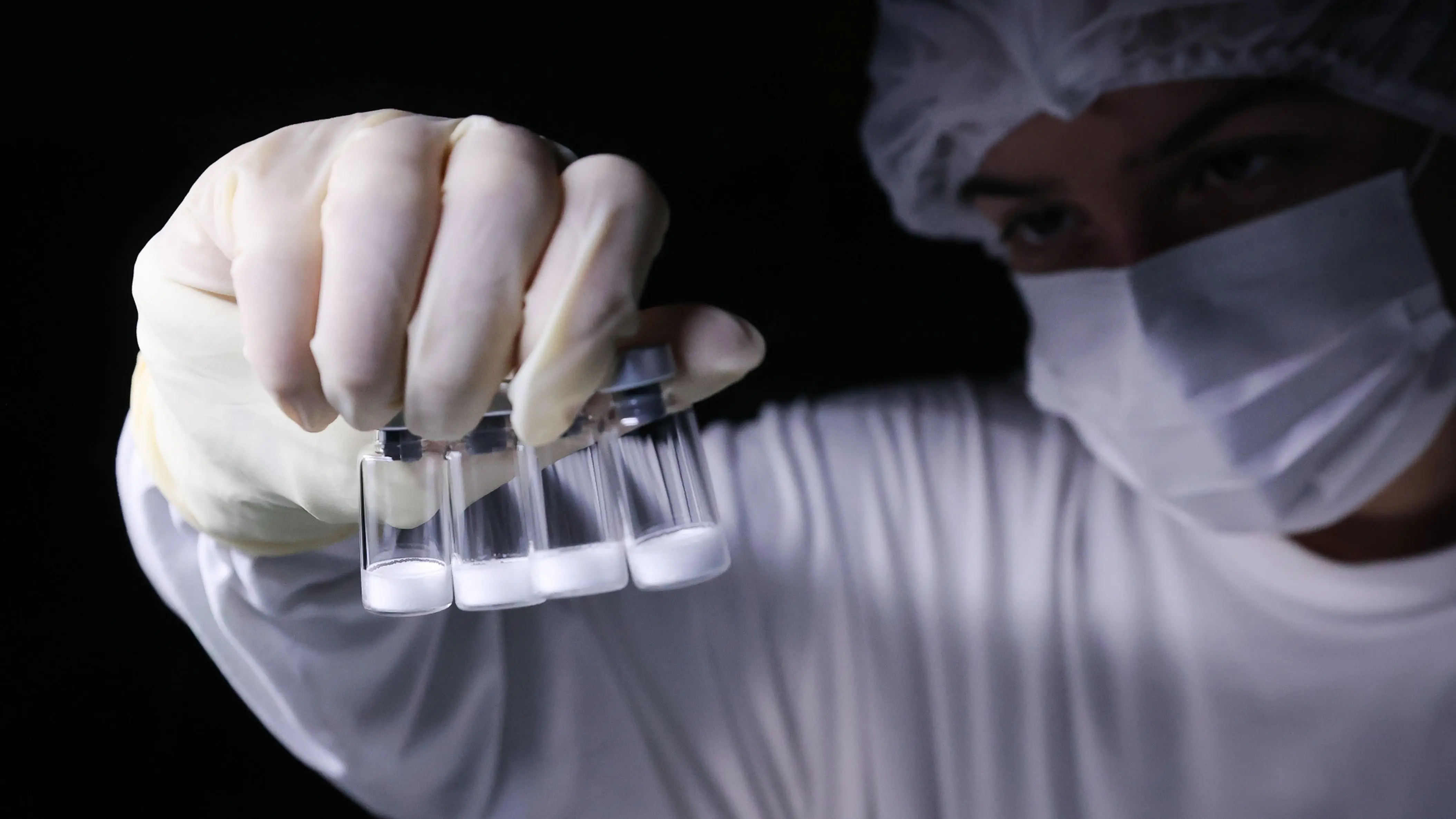 Pesquisador manipula frascos em laboratório, etapa essencial no desenvolvimento de vacinas como a do Instituto Butantan, que reforça as estratégias do Governo de São Paulo no combate à dengue.