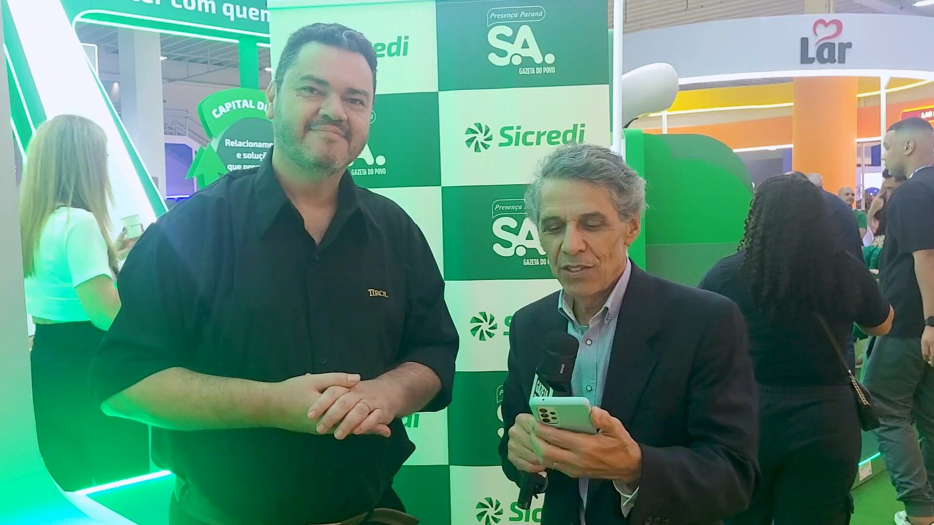 O jornalista Celio Martins entrevista Rodney Guariza, gerente de marketing da Tirol, durante a Expoapras 2026, sobre lançamentos saudáveis, inovação no setor de lácteos e expansão da marca no Paraná.