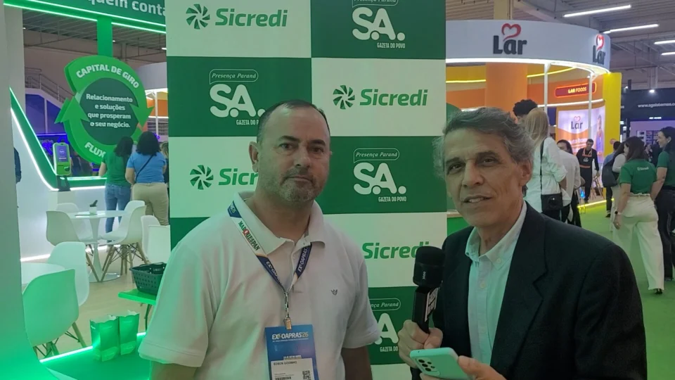 O jornalista Celio Martins entrevista Edson Godinho, da Advocacia Edson Godinho, no estande do Sicredi durante a Expoapras 2026, sobre atendimento próximo, tecnologia e apoio ao crescimento empresarial.