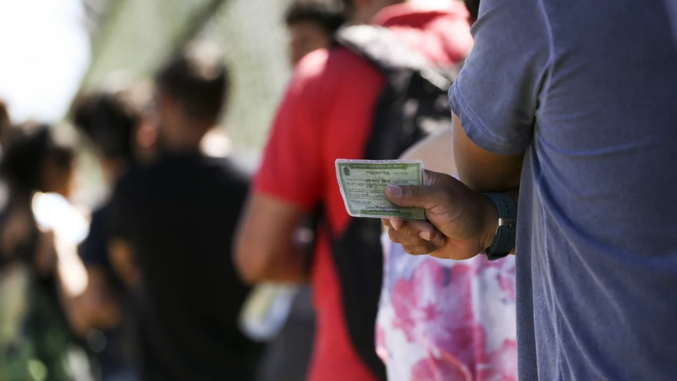 Pessoa em uma fila com o título de eleitor na mão, para fazer a regularização.