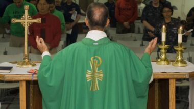 Imagem mostra um padre durante um momento de fé e oração em uma missa.