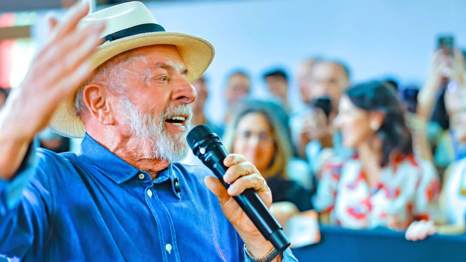 Presidente Luiz Inácio Lula da Silva discursando em púlpito oficial. A imagem ilustra a análise sobre como o conflito no Oriente Médio mascara o déficit primário e os problemas estruturais das contas públicas brasileiras em 2026.