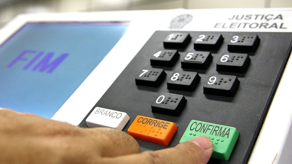 Pessoa votando na urna eletrônica e apertando o botão Confirma