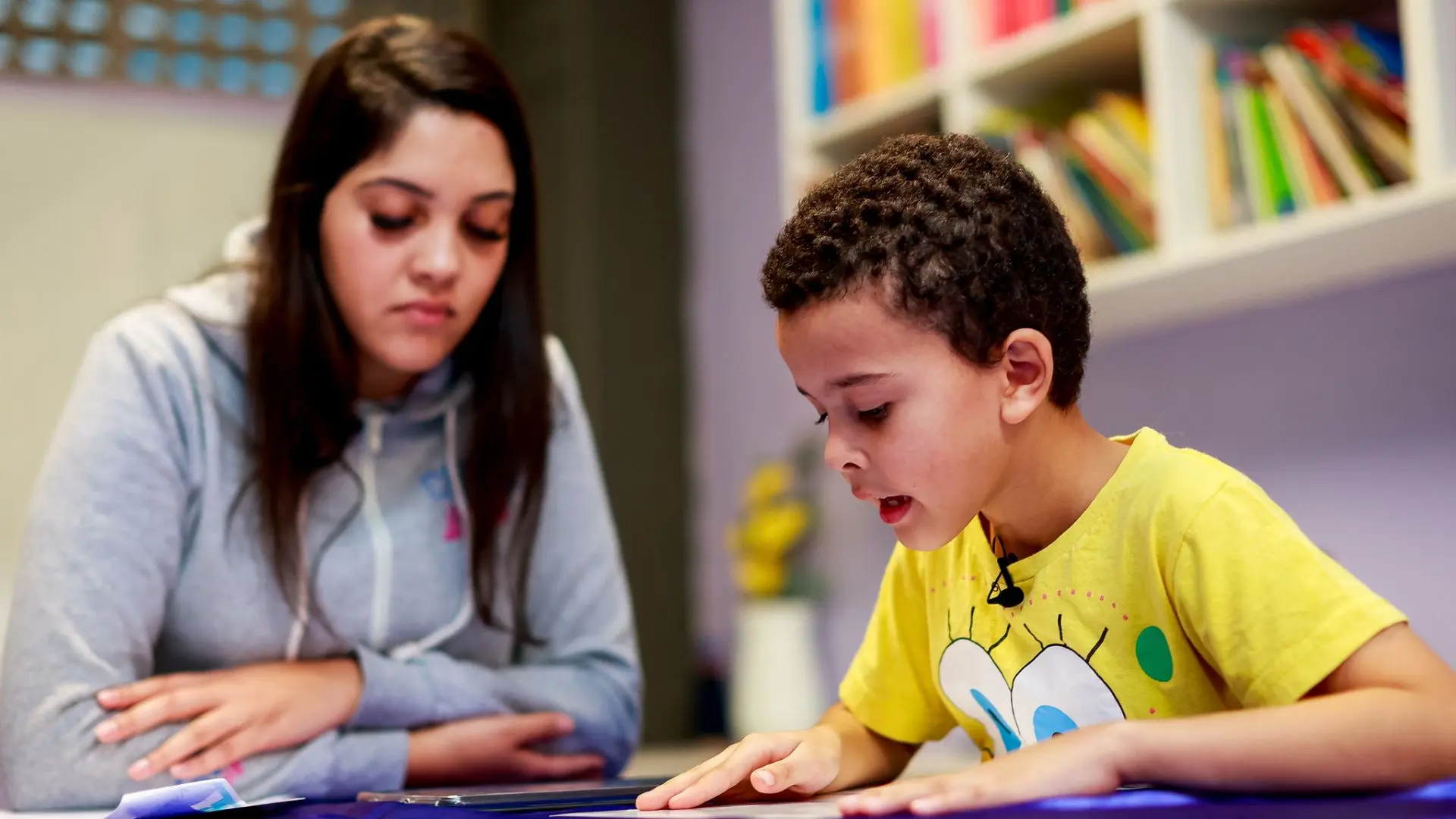Aluno em processo de leitura com acompanhamento pedagógico, com foco no desenvolvimento da alfabetização na idade certa e no apoio individualizado nas escolas públicas paulistas.