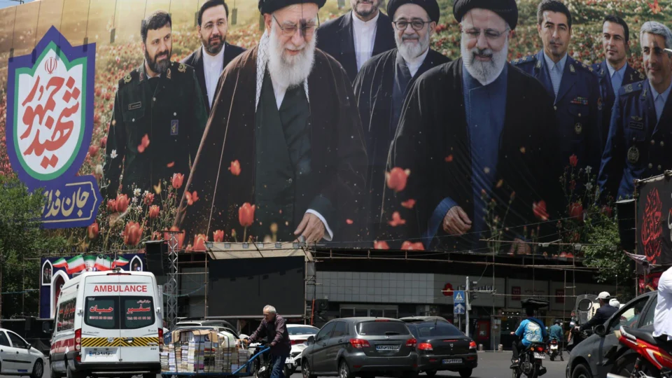 Trabalhador passa diante de outdoor com imagens de Ali Khamenei e Ebrahim Raisi, na praça Enghelab, em Teerã, em meio à continuidade das tensões entre Irã e Estados Unidos.