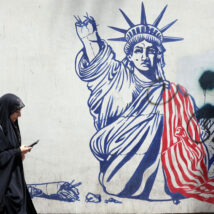 Mulher passa em frente a um mural anti-EUA em Teerã, capital do Irã. Imagem referente a matéria