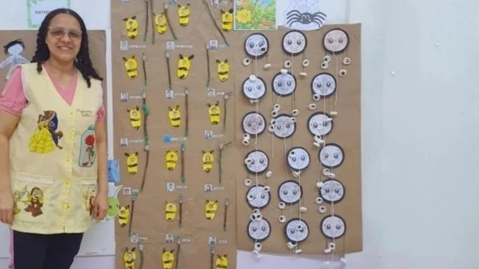 Uma professora em pé ao lado de um painel com os animais estudados no projeto descrito.