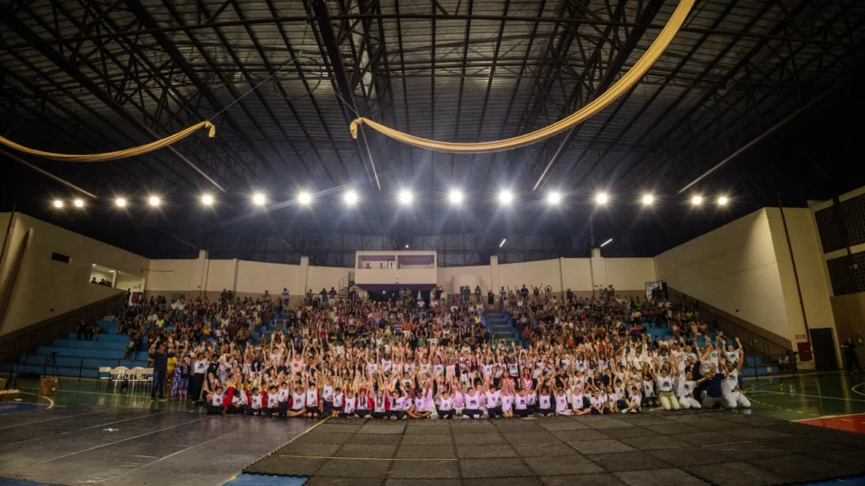 Foto em uma quadra coberta, com pessoas sentadas ao fundo