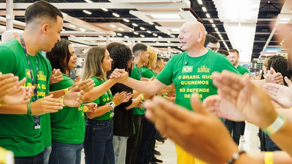 Luciano Hang com camiseta verde da Havan cumprimenta pessoas com camisetas da mesma marca no interior da loja.