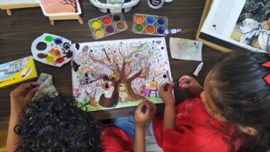 Duas crianças pintando uma folha de papel com tinta