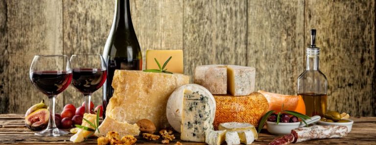Various types of cheese, glasses and bottle of red wine placed on wooden table, copyspace for text. Wooden planks on background