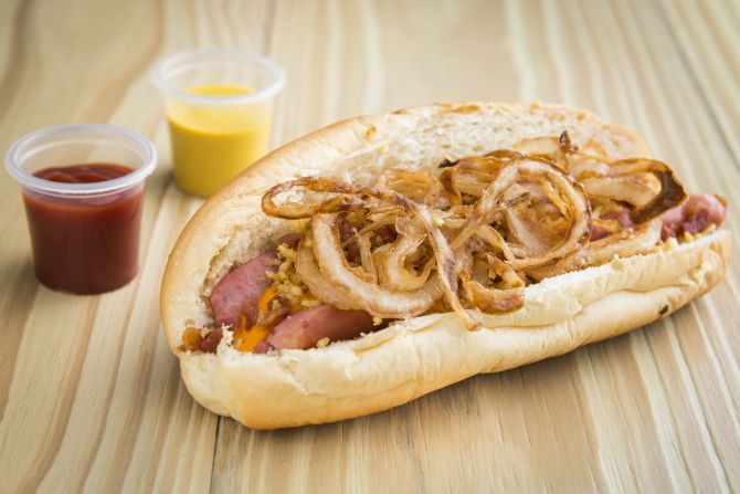 Hot Dog Kharina: salsicha de carnes bovina e suína com cebola frita, molho cheddar e farofa. Foto: Letícia Akemi/Gazeta do Povo Hot Dog Kharina: salsicha de carnes bovina e suína com cebola frita, molho cheddar e farofa. Foto: Letícia Akemi/Gazeta do Povo