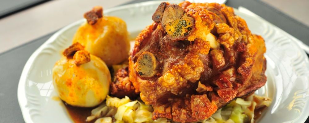 Joelho de porco assado à pururuca acompanha dois bolinhos de batata, chucrute, repolho roxo e salsicha Bratwurst. Serve duas pessoas (R$ 97,90). (Foto: Divulgação)