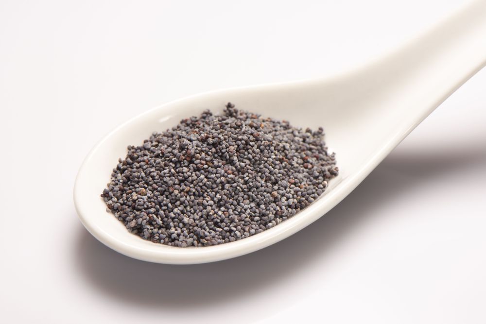 Pile of poppy seeds in white ceramic spoon on white background Pile of poppy seeds in white ceramic spoon on white background