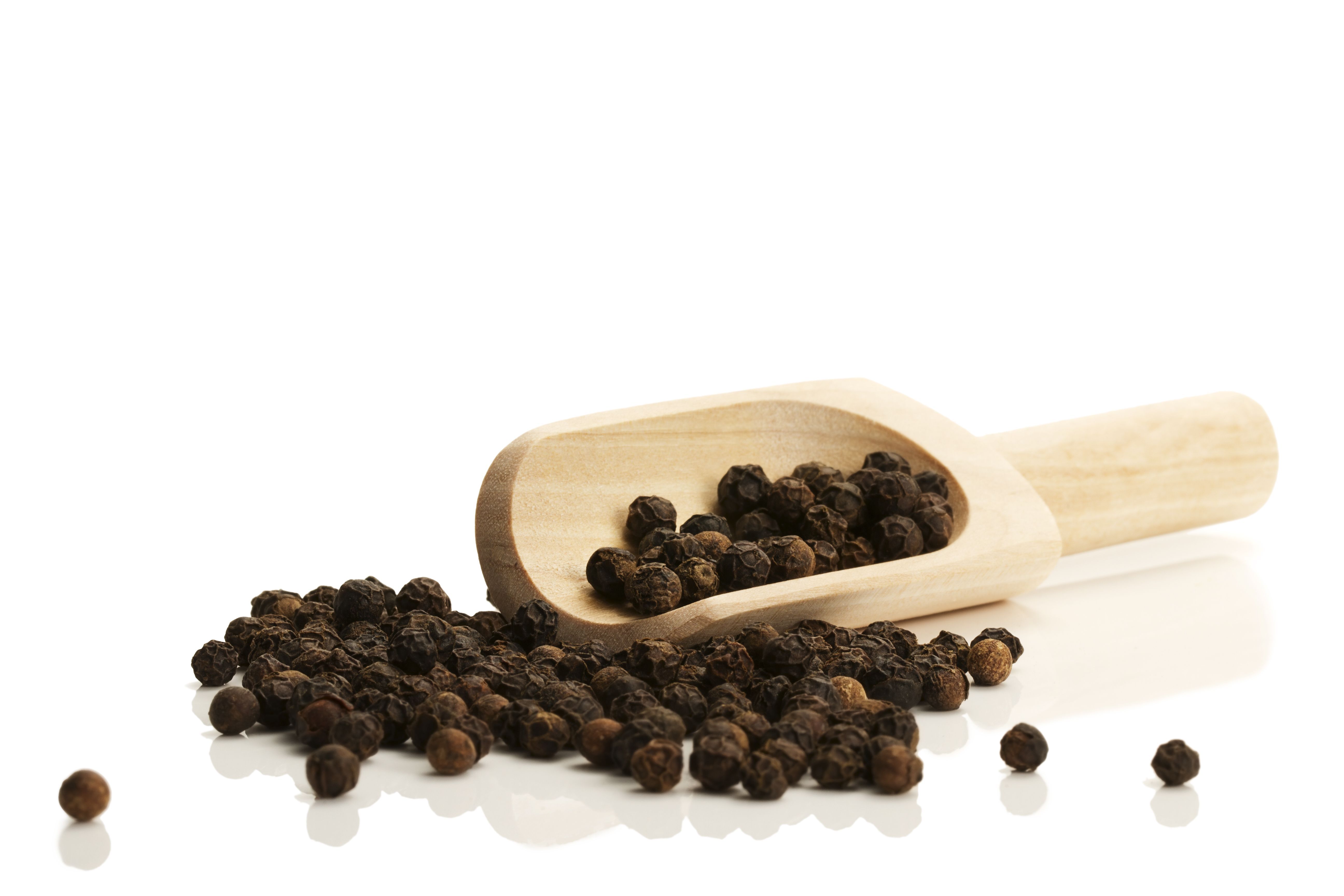 black peppercorns with a small wooden shovel from side on white background black peppercorns with a small wooden shovel from side on white background