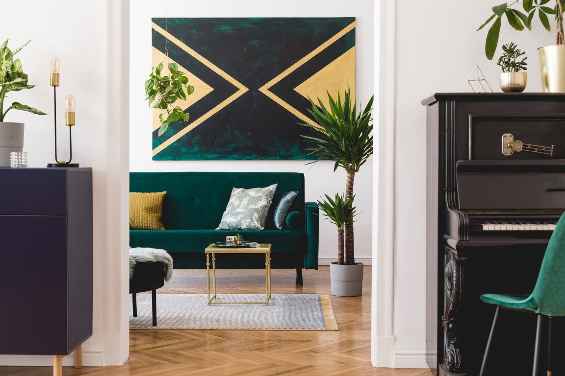 Stylish luxury home interior of sitting room with green velvet sofa, coffee table, shelf, piano, pouf, tropical plants, pillows and elegant accessories. Modern and cozy home decor. Template. Stylish luxury home interior of sitting room with green velvet sofa, coffee table, shelf, piano, pouf, tropical plants, pillows and elegant accessories. Modern and cozy home decor. Template.