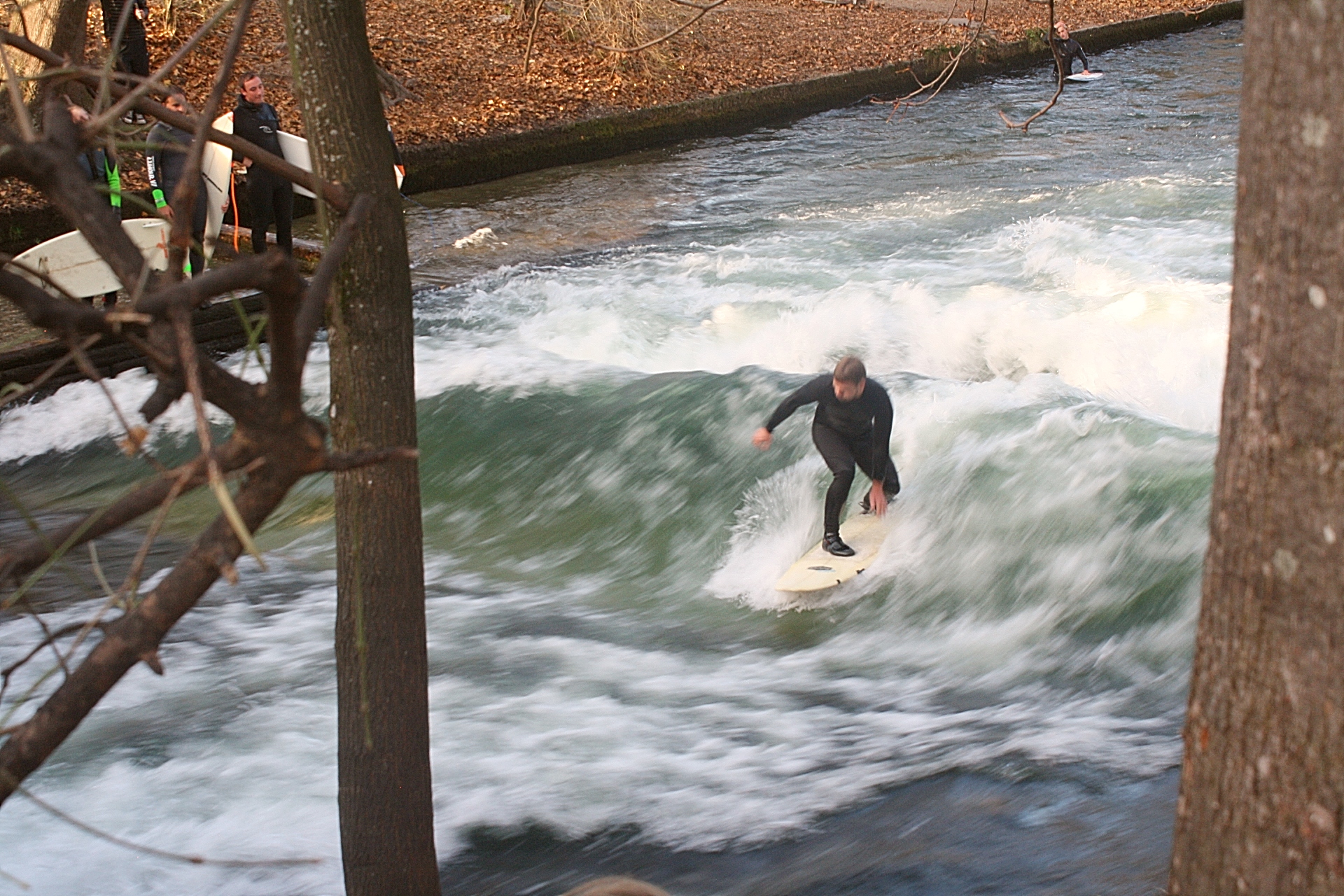 Homem surfa no canal de um dos parques de Munique enquanto outros aventureiros aguardam sua vez. Foto: Carolina Werneck/Gazeta do Povo Homem surfa no canal de um dos parques de Munique enquanto outros aventureiros aguardam sua vez. Foto: Carolina Werneck/Gazeta do Povo