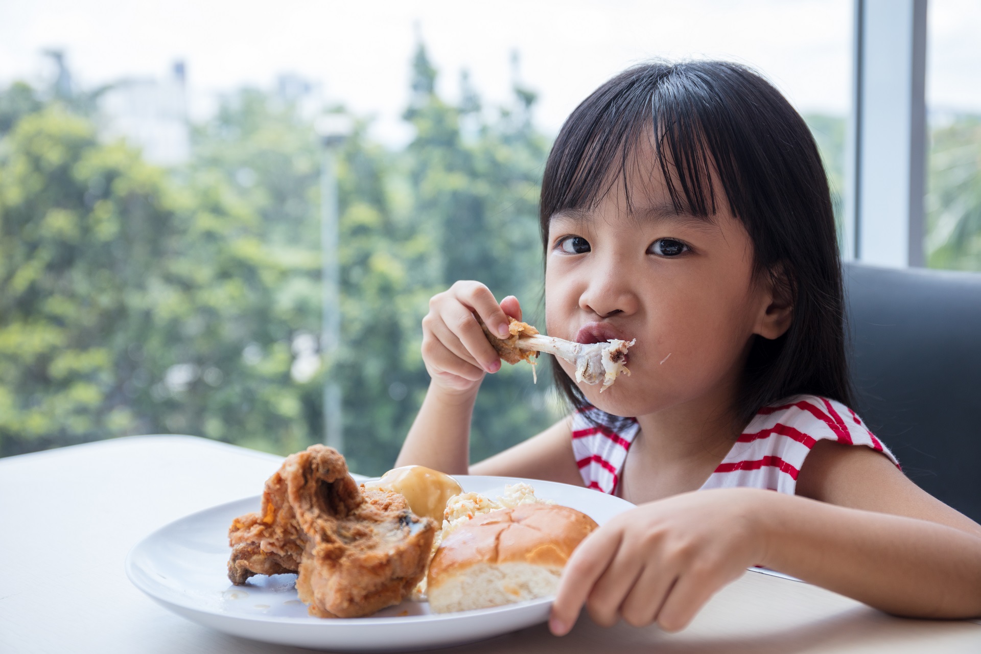Asian Chinese little girl eating fried chicken at indoor restaurant