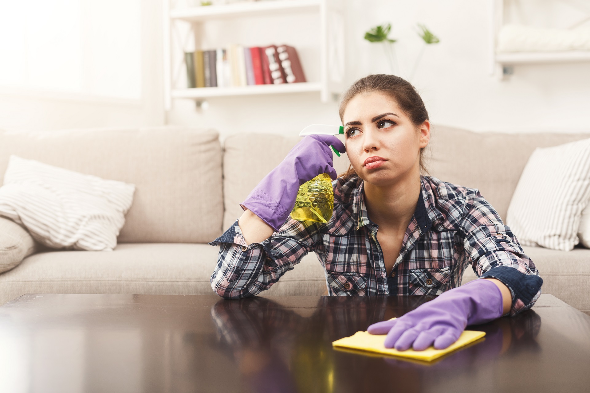 Dreaming woman using spray cleaner on wooden surface. Sad and tired girl cleaning furniture, housework and chores concept, copy space Dreaming woman using spray cleaner on wooden surface. Sad and tired girl cleaning furniture, housework and chores concept, copy space